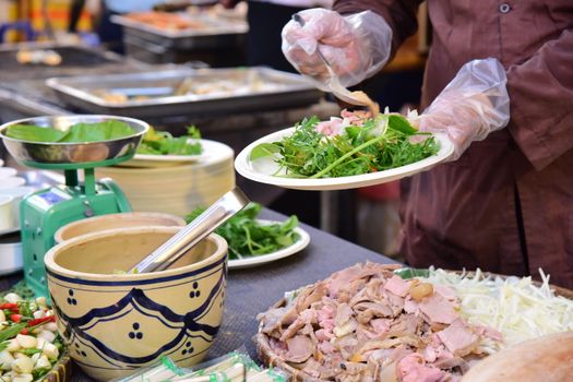Street vendor preparing fresh salad with meat and vegetables at outdoor food market.