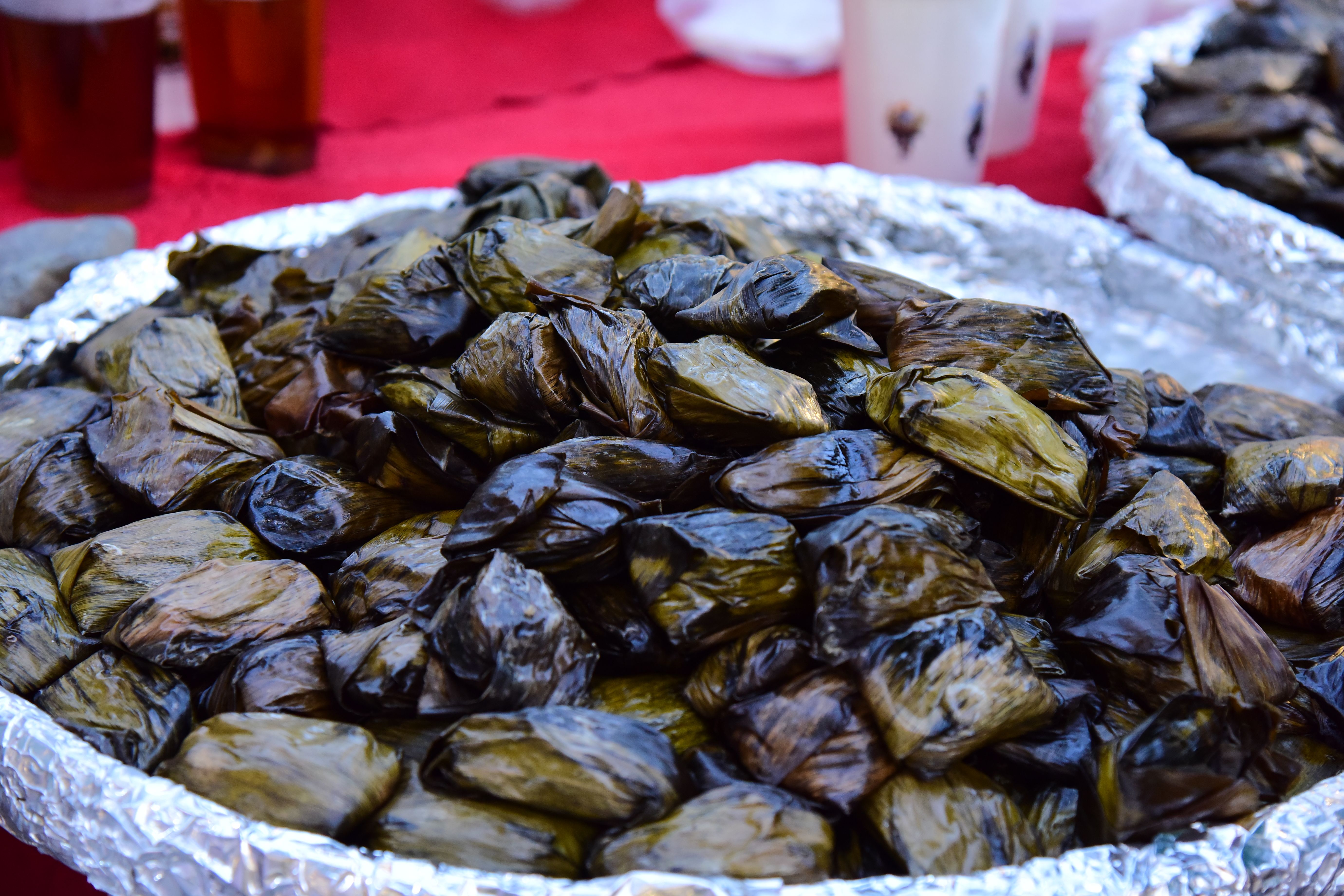 Close-up of traditional snacks wrapped in green leaves on a foil tray, ready for a festive occasion.