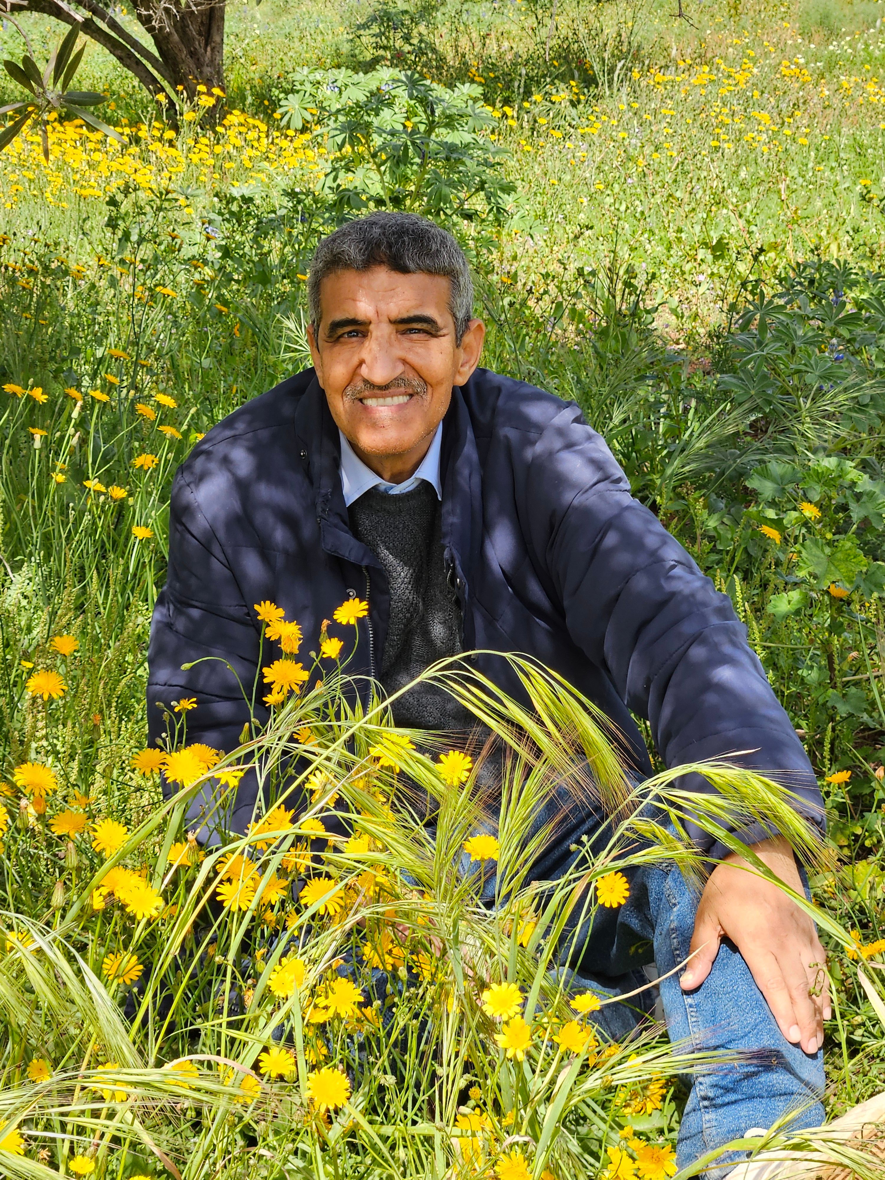 A middle-aged man smiling while sitting in a vibrant field of yellow spring flowers.