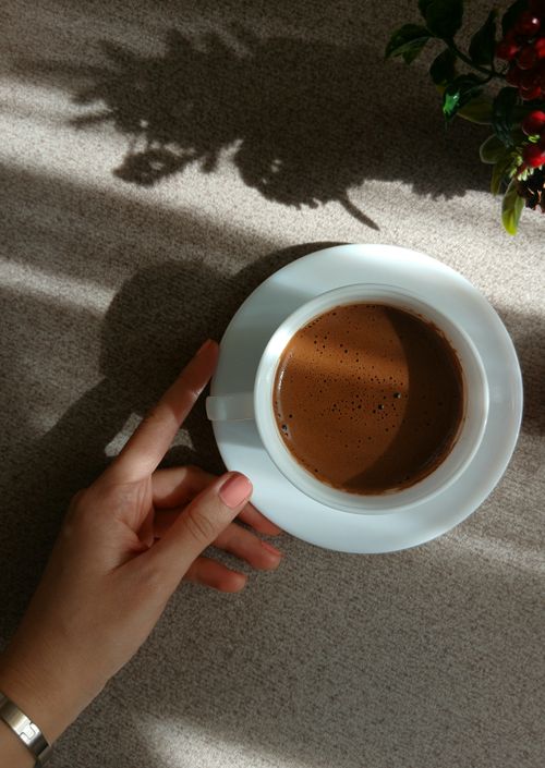 Free A hand delicately holding a coffee cup on a sunlit table with light shadows. Stock Photo