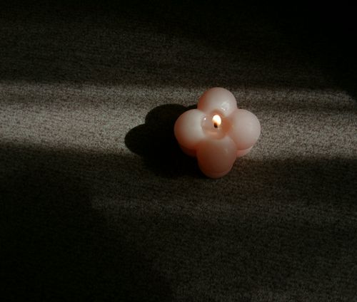 Free A solitary flower-shaped candle casting shadows in a dimly lit room. Stock Photo
