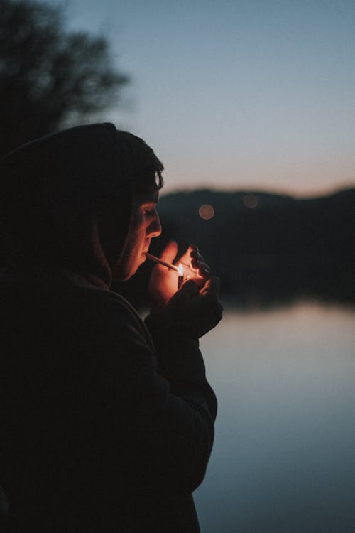 Man in Black Hoodie Smoking Cigarette on Front of Lake