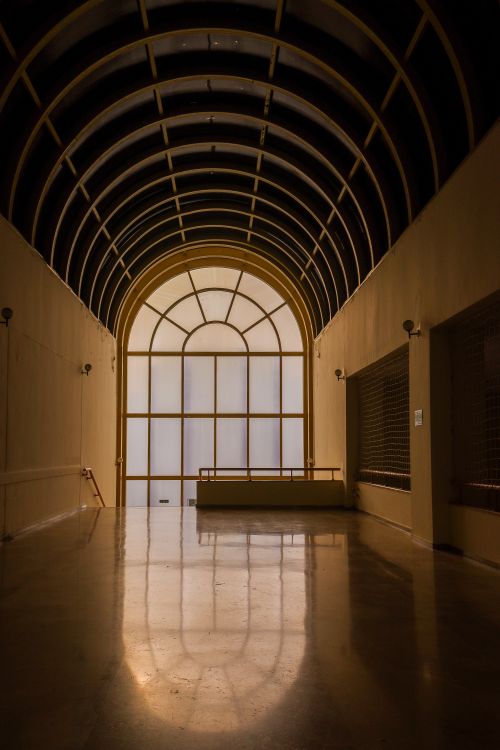 Free A serene, arched hallway with warm lighting and reflective flooring creates an elegant atmosphere. Stock Photo