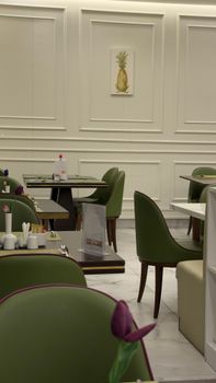 Stylish indoor cafe setting with green chairs, white walls, and a pineapple artwork.