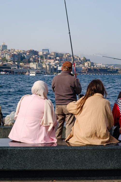 Free A group of people fishing by the Bosphorus with a cityscape backdrop under clear skies. Stock Photo