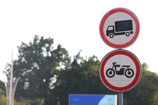 Traffic signs against a backdrop of trees in Uzbekistan, prohibiting trucks and motorcycles.