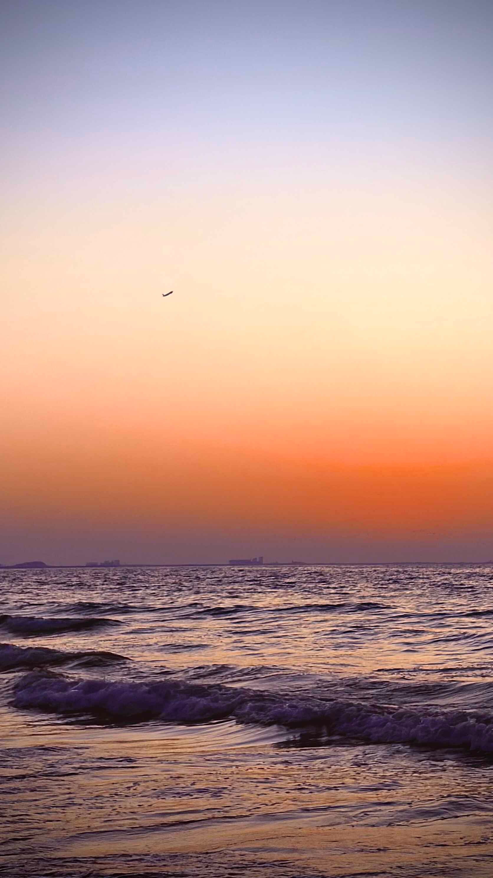 夕阳西下，海面波光粼粼，远处有飞机飞过，景色优美，营造出宁静祥和的氛围。