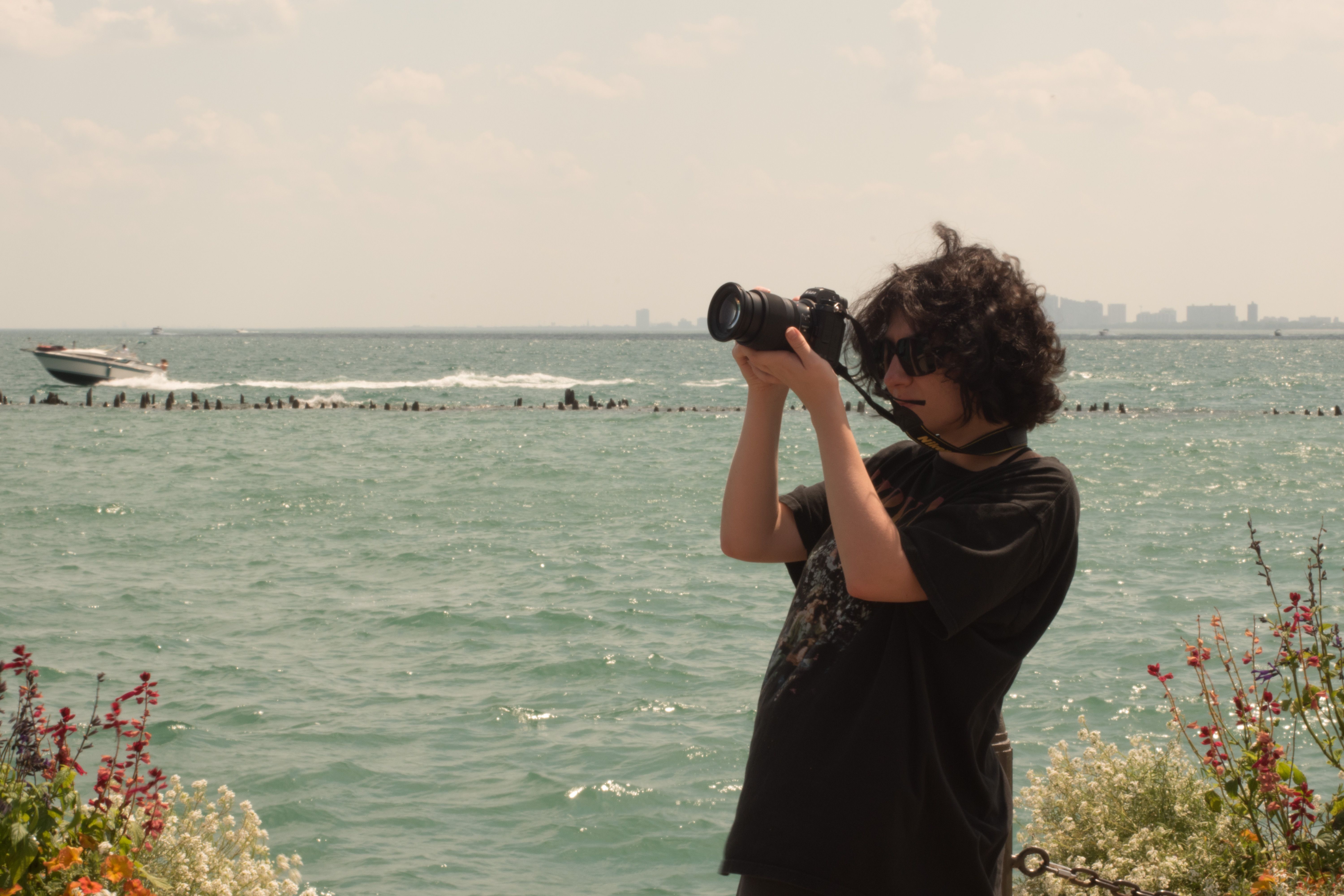 A person photographing a tranquil seaside scene with a DSLR camera on a sunny day.