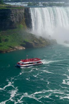 A vibrant tourist boat sails near the majestic Niagara Falls waterfall on a sunny day.