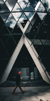A man walks past the modern architecture of the Gherkin building facade in London.