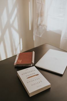 A minimalist workplace setup with a laptop, books, and natural light.