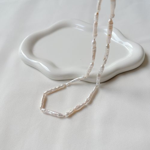Free Minimalist image of a freshwater pearl necklace on a white dish, showcasing elegance and simplicity. Stock Photo