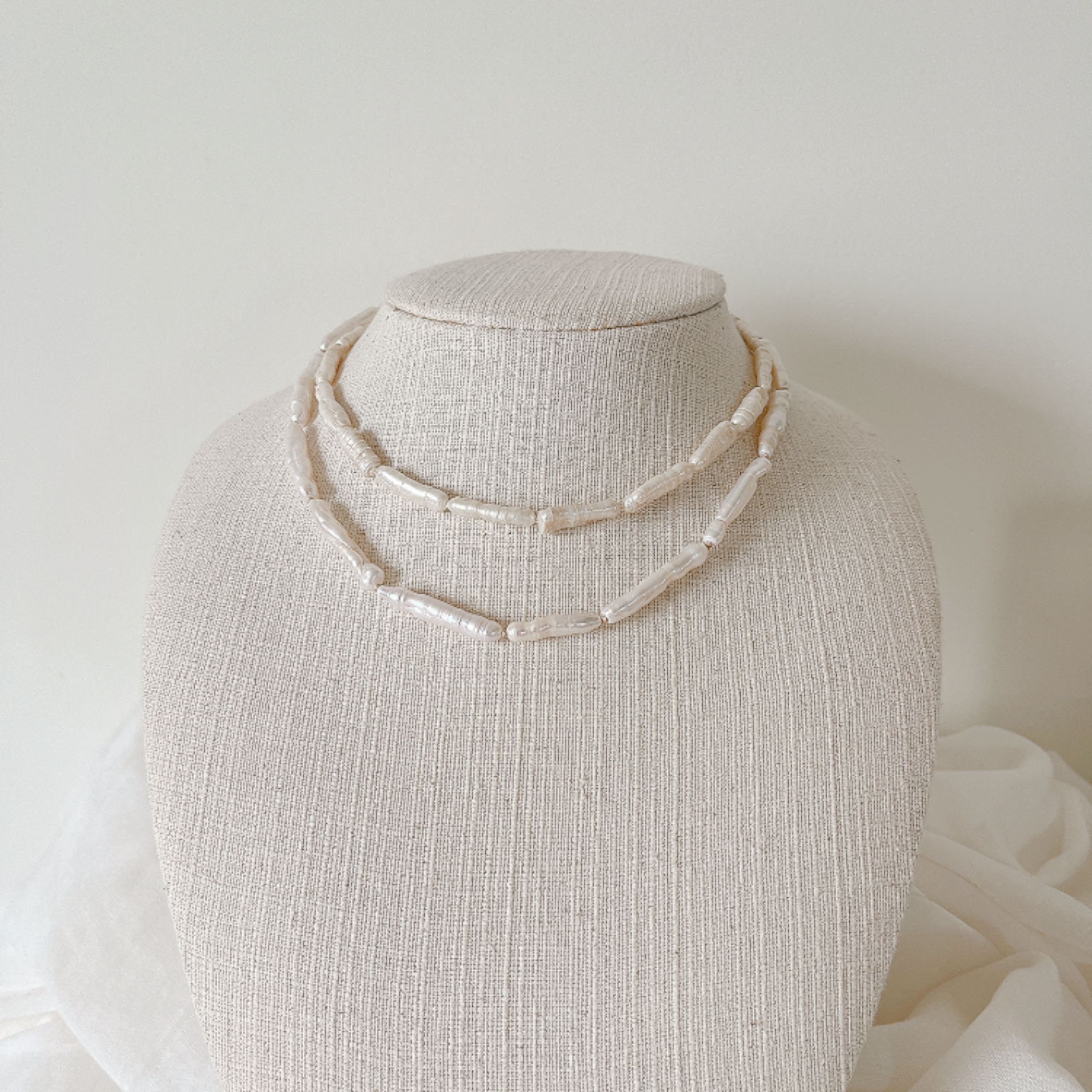 Two-row rice pearl necklace on a linen display bust