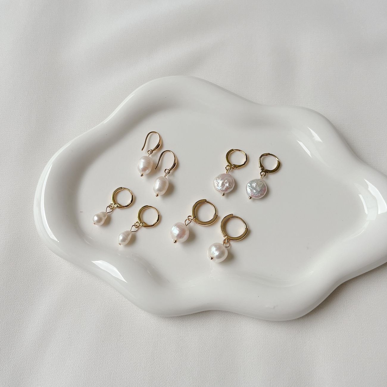 A collection of elegant pearl earrings displayed on a white ceramic tray, offering a minimalist style.