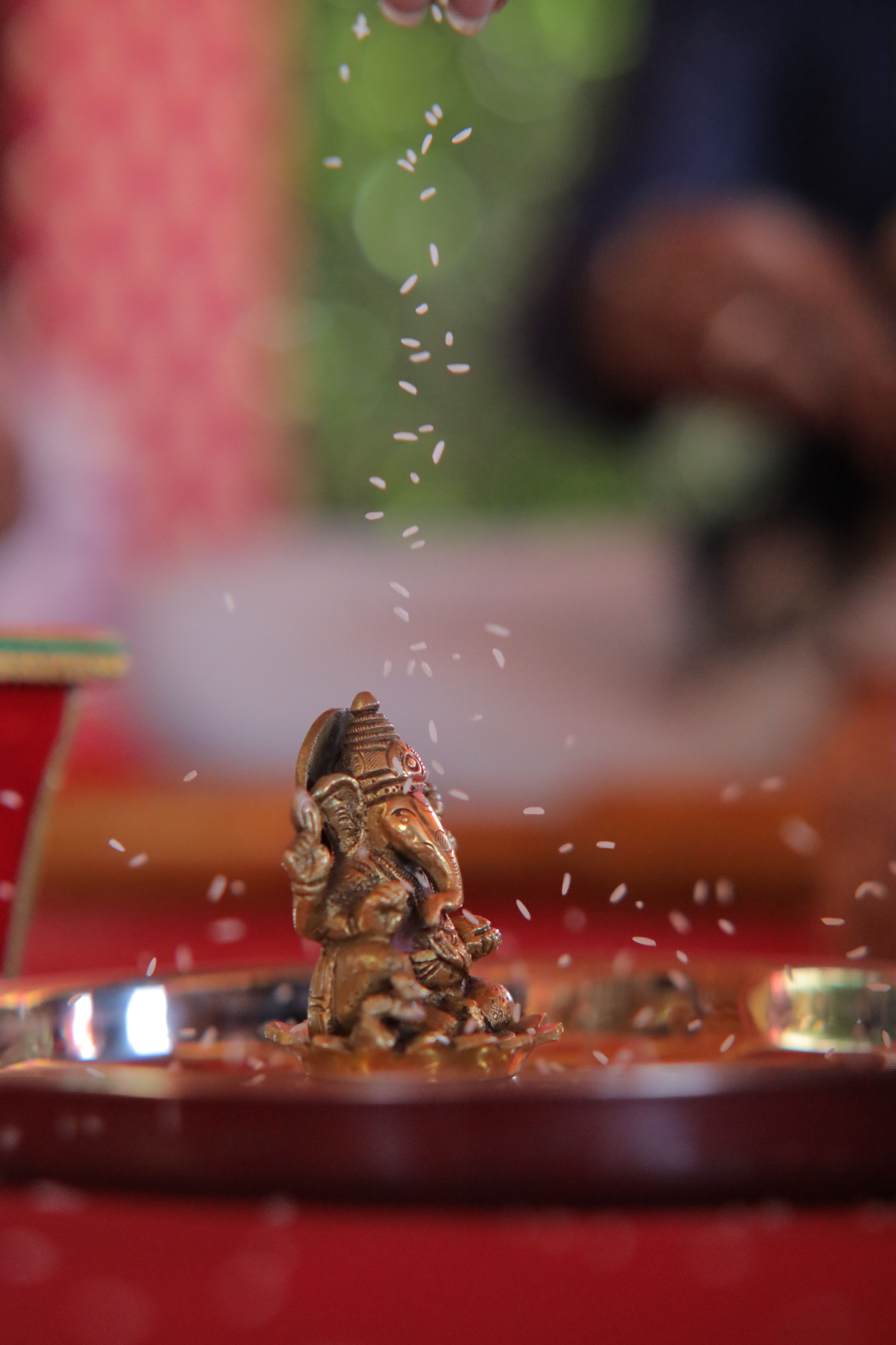 Close-up of a Ganesh statue with rice being sprinkled during a Hindu ritual ceremony.