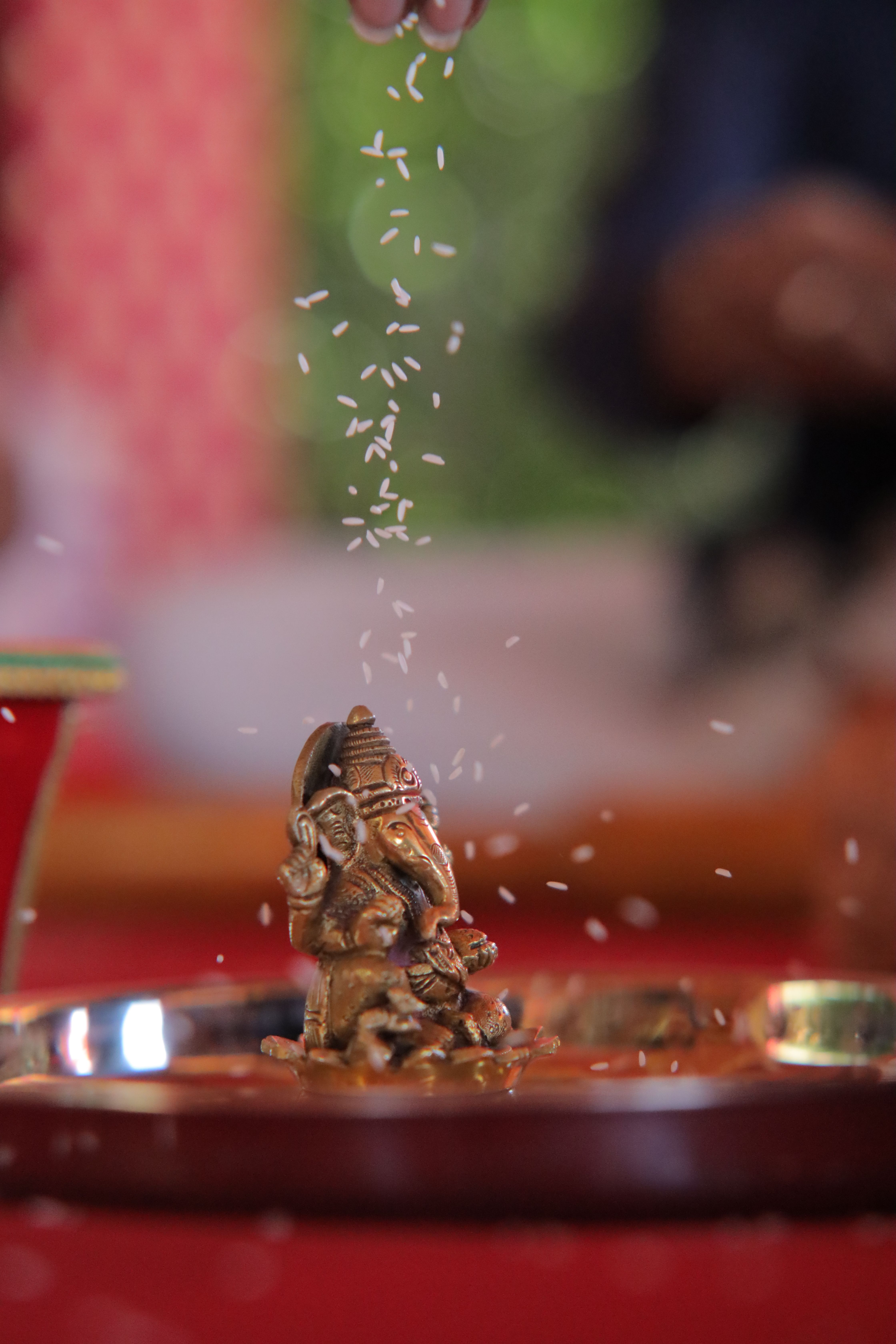 A small Ganesh statue on a tray with rice raining down during a traditional ceremony.