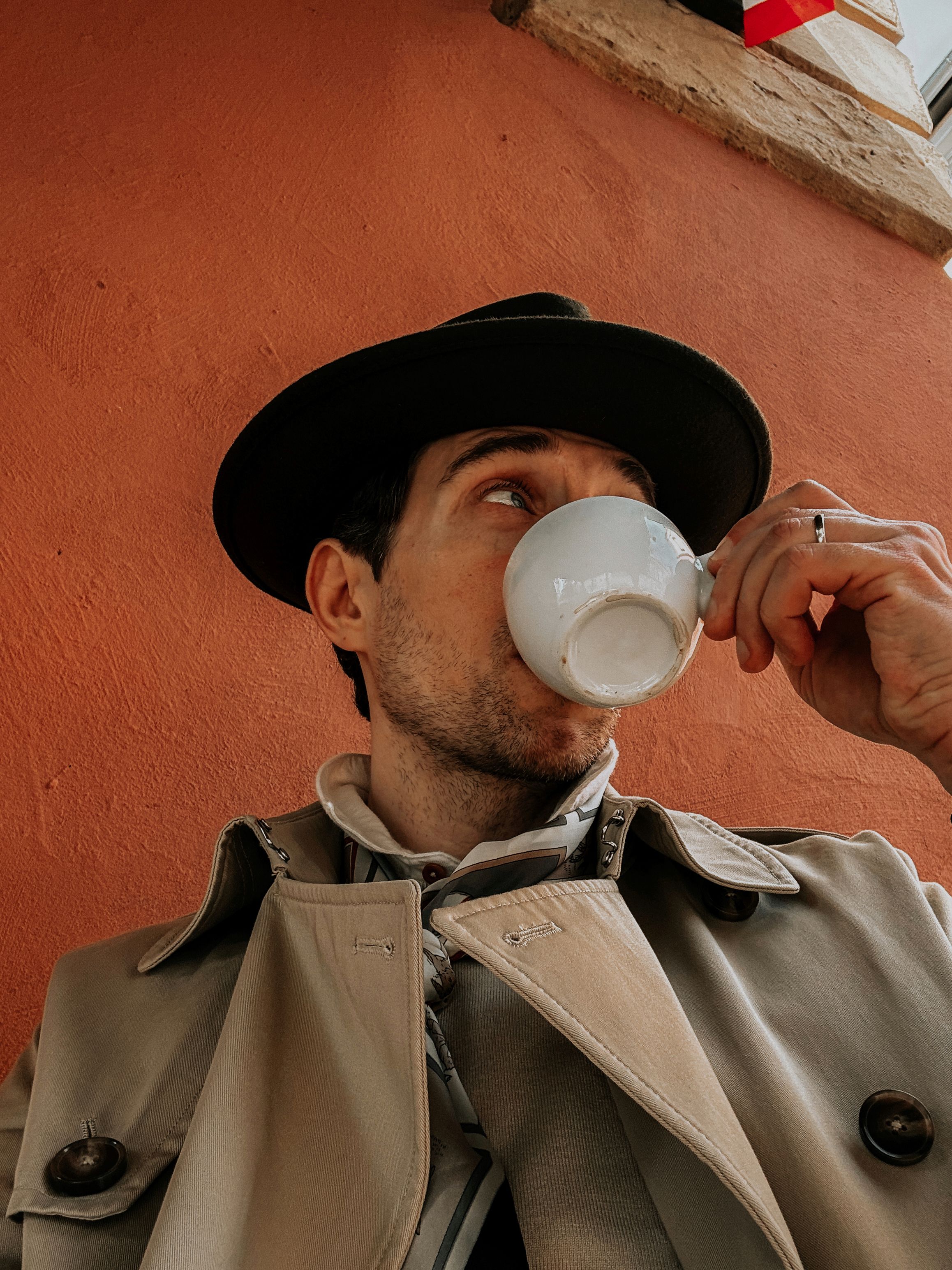 Um homem fashionista desfruta de café contra uma parede laranja texturizada na Baixa Silésia.