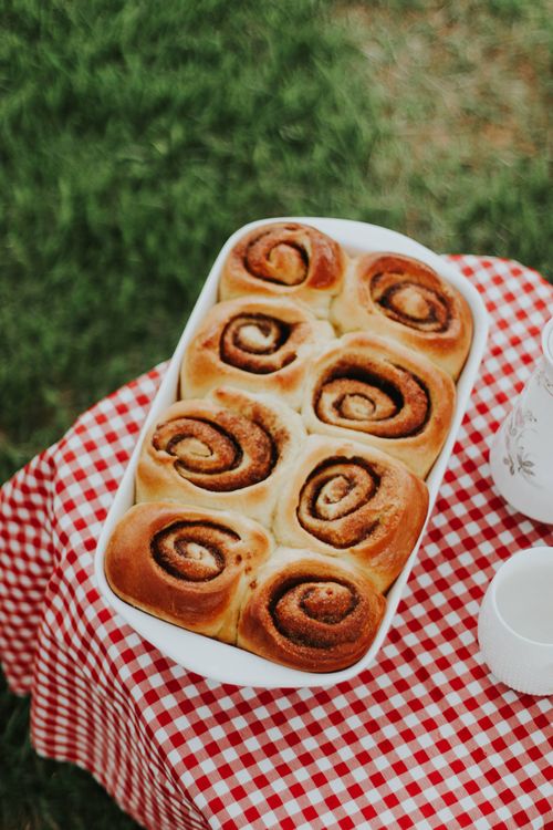 Free Delicious homemade cinnamon rolls in a white dish on a checkered picnic tablecloth outdoors. Stock Photo