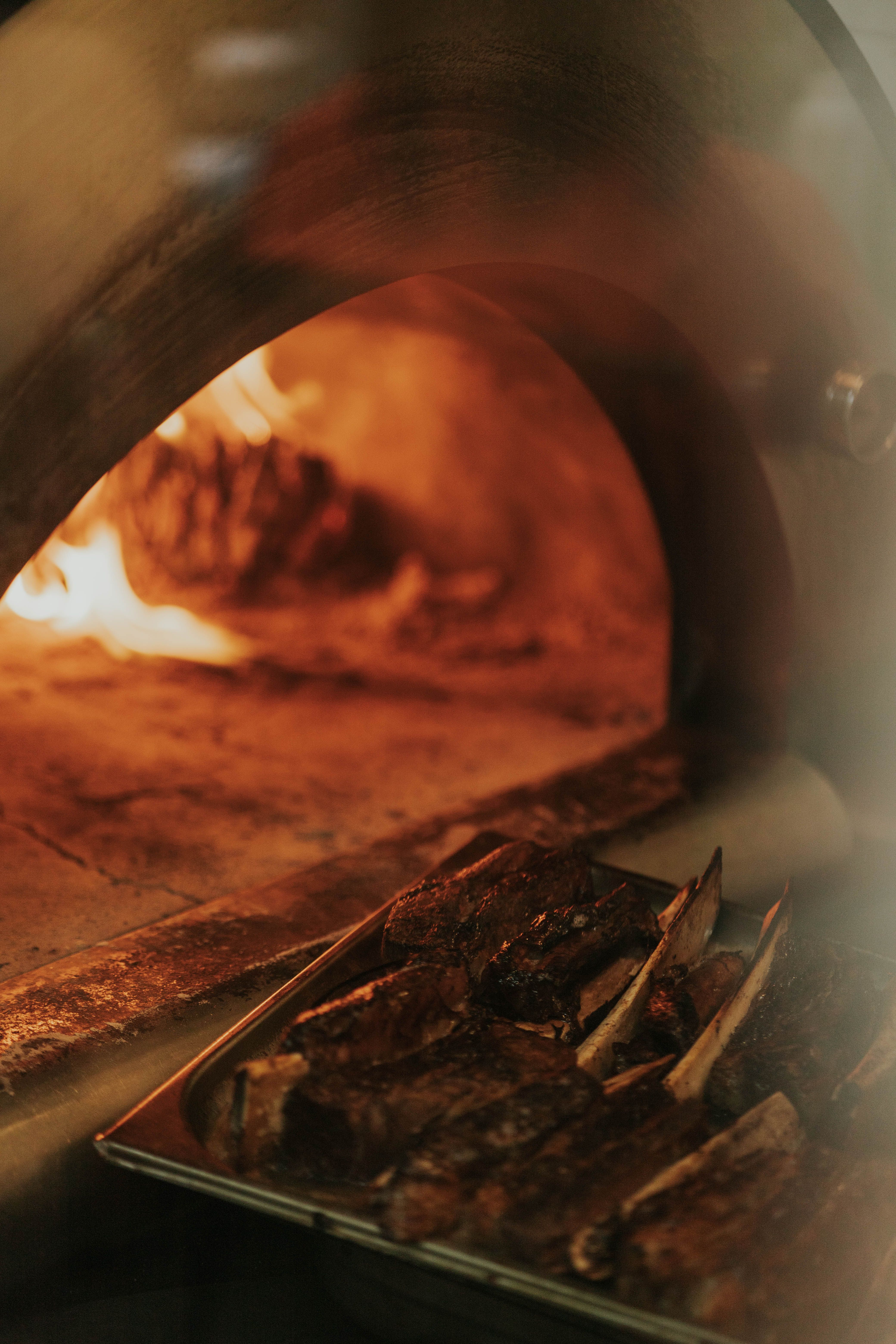 Glazed ribs resting in the wood-fired oven with oak flames visible behind them