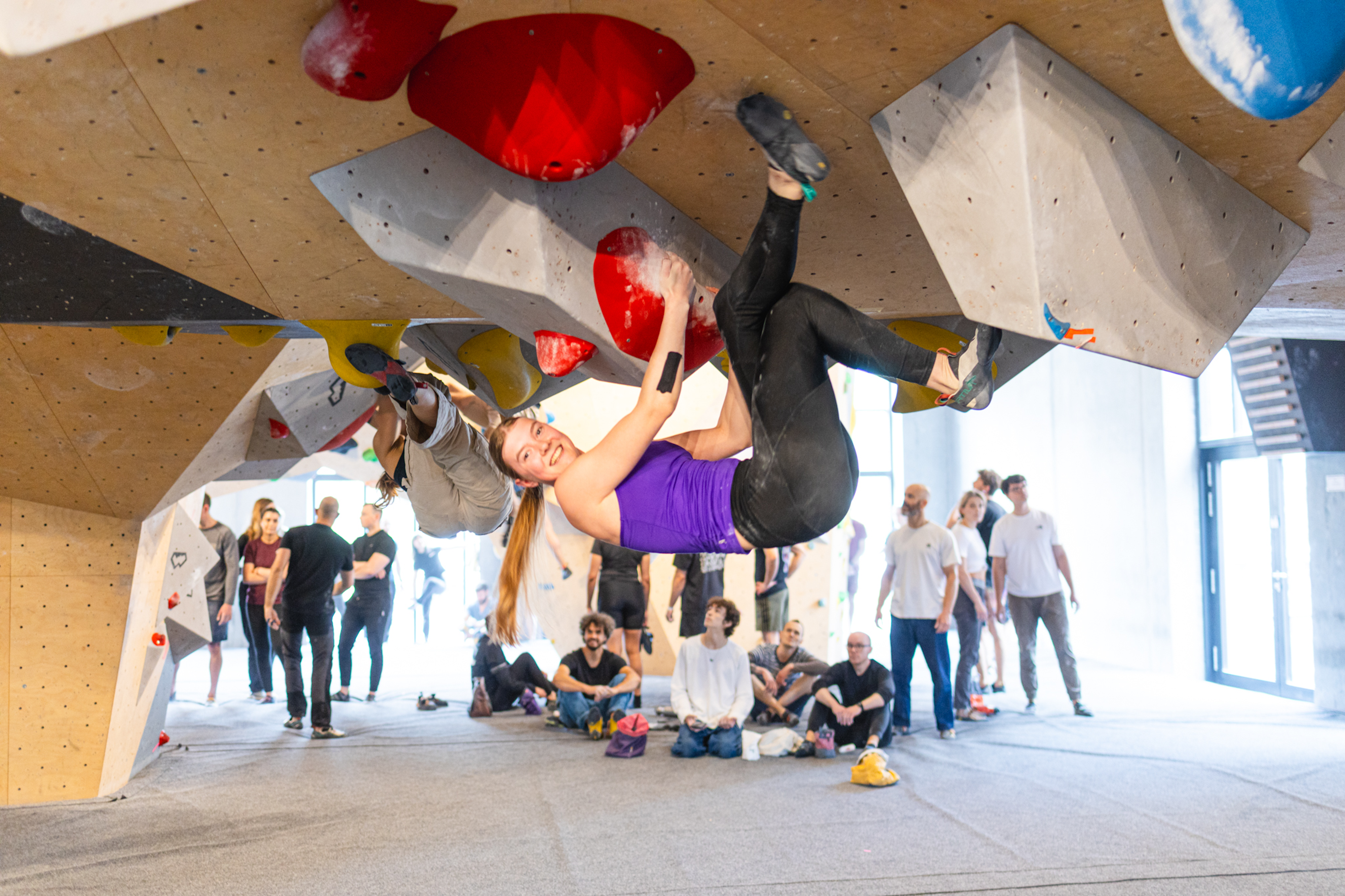 A female athlete climbs a bouldering wall during an indoor climbing competition.