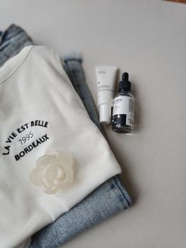 Flat lay of white top with skincare products and denim jeans for a casual look.
