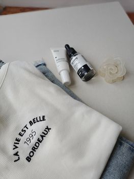 Flat lay of skincare products with a trendy Bordeaux embroidery sweater.