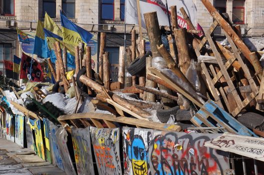 A vibrant urban barricade constructed with wood and tires, adorned with colorful flags and graffiti.