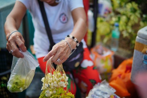 Free An outdoor scene of a street vendor selecting flowers and fruits, representing local market culture. Stock Photo