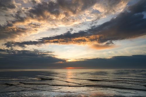 Free Peaceful ocean scene at sunset with dramatic clouds and gentle waves. Stock Photo
