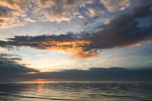 Free Dramatic sunset sky with vibrant clouds over a calm ocean surface, creating a peaceful seascape scene. Stock Photo