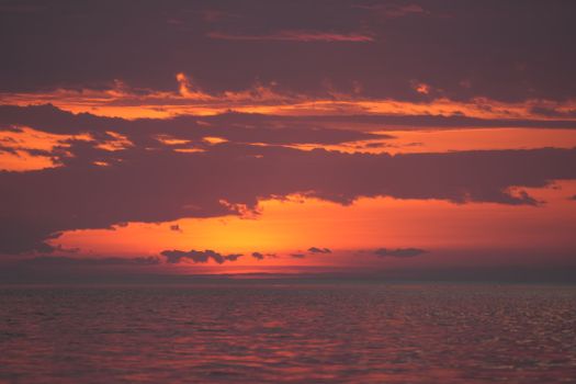 Vibrant sunset casting orange and red hues over tranquil ocean waves.