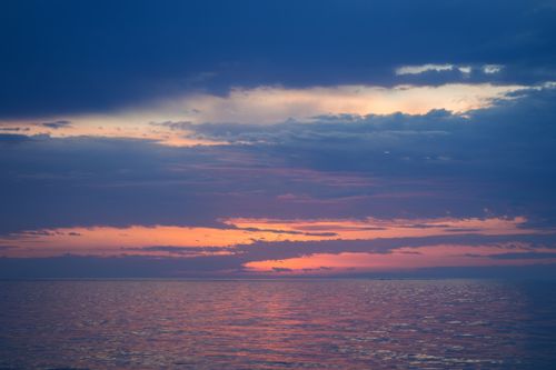 Free Stunning sunset over calm ocean waters with vibrant colors and dramatic clouds. Stock Photo