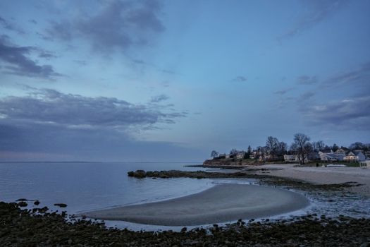 Tranquil waterfront view at dusk with clouds and coastal homes in the distance.