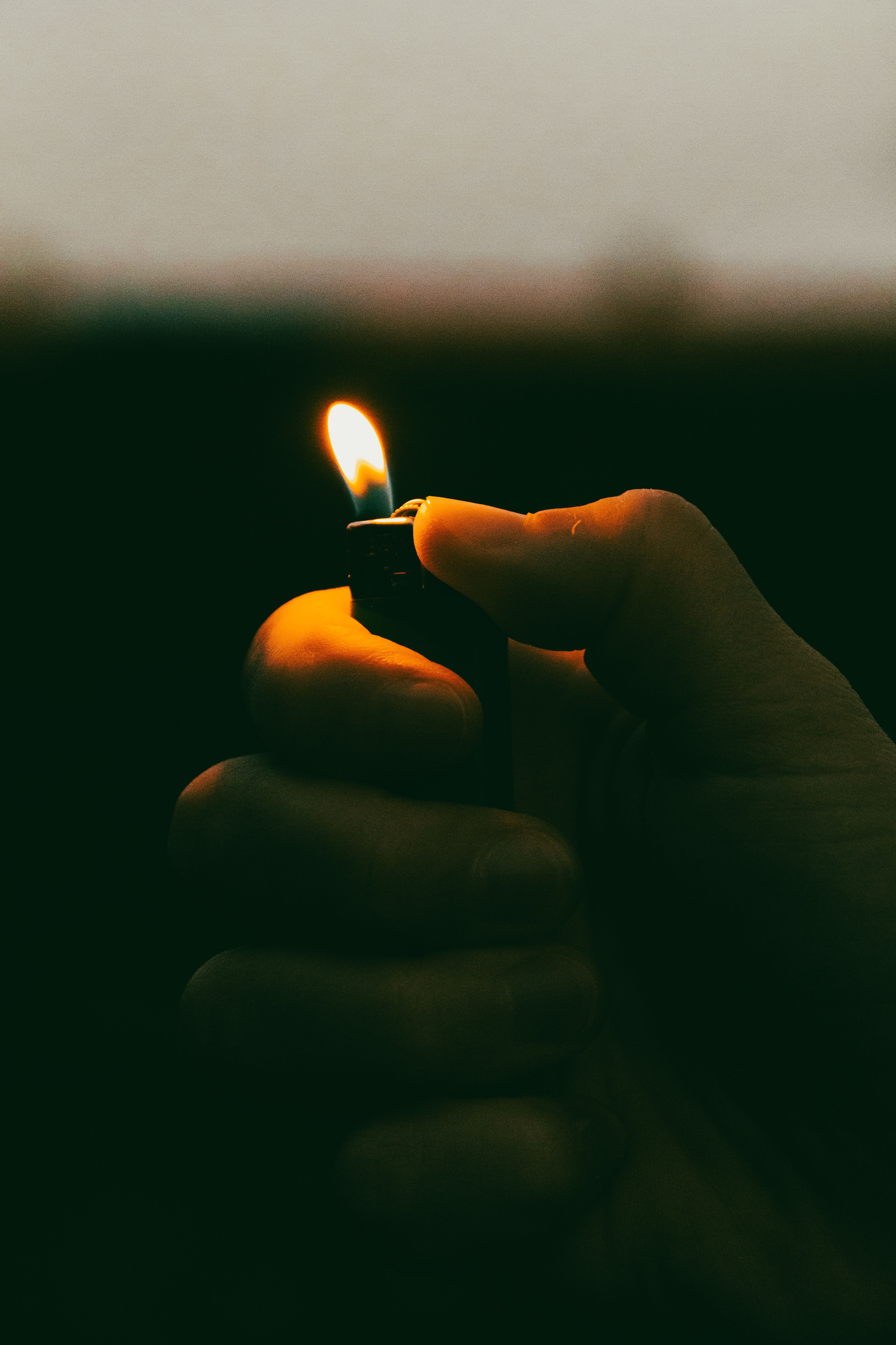 A close-up shot of a hand holding a lit lighter, casting warm light in dark surroundings.
