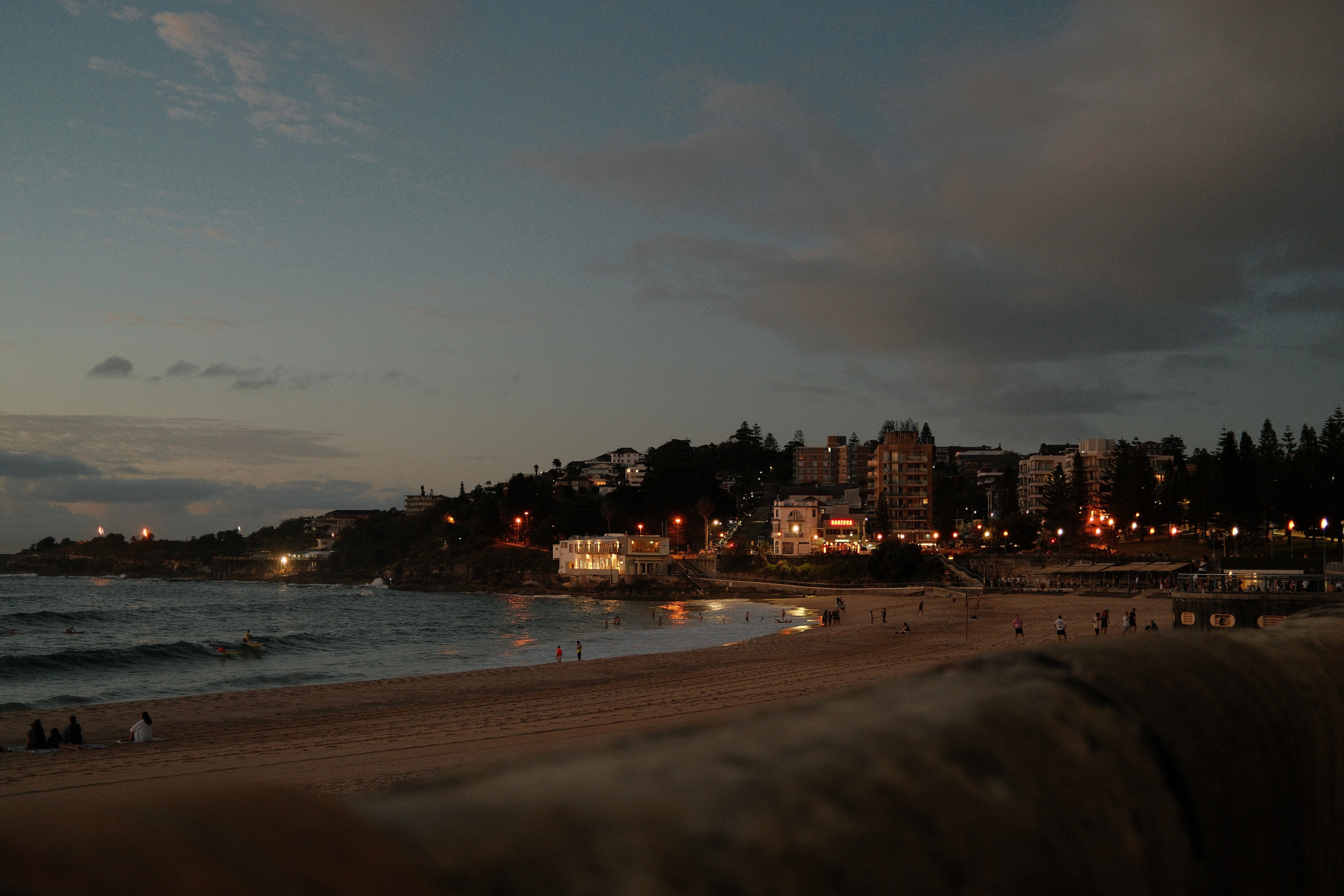 Evening view of a beachfront cityscape in Sydney, Australia with twinkling lights.