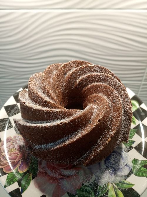 Free A beautifully swirled chocolate bundt cake topped with powdered sugar, displayed on a floral plate. Stock Photo
