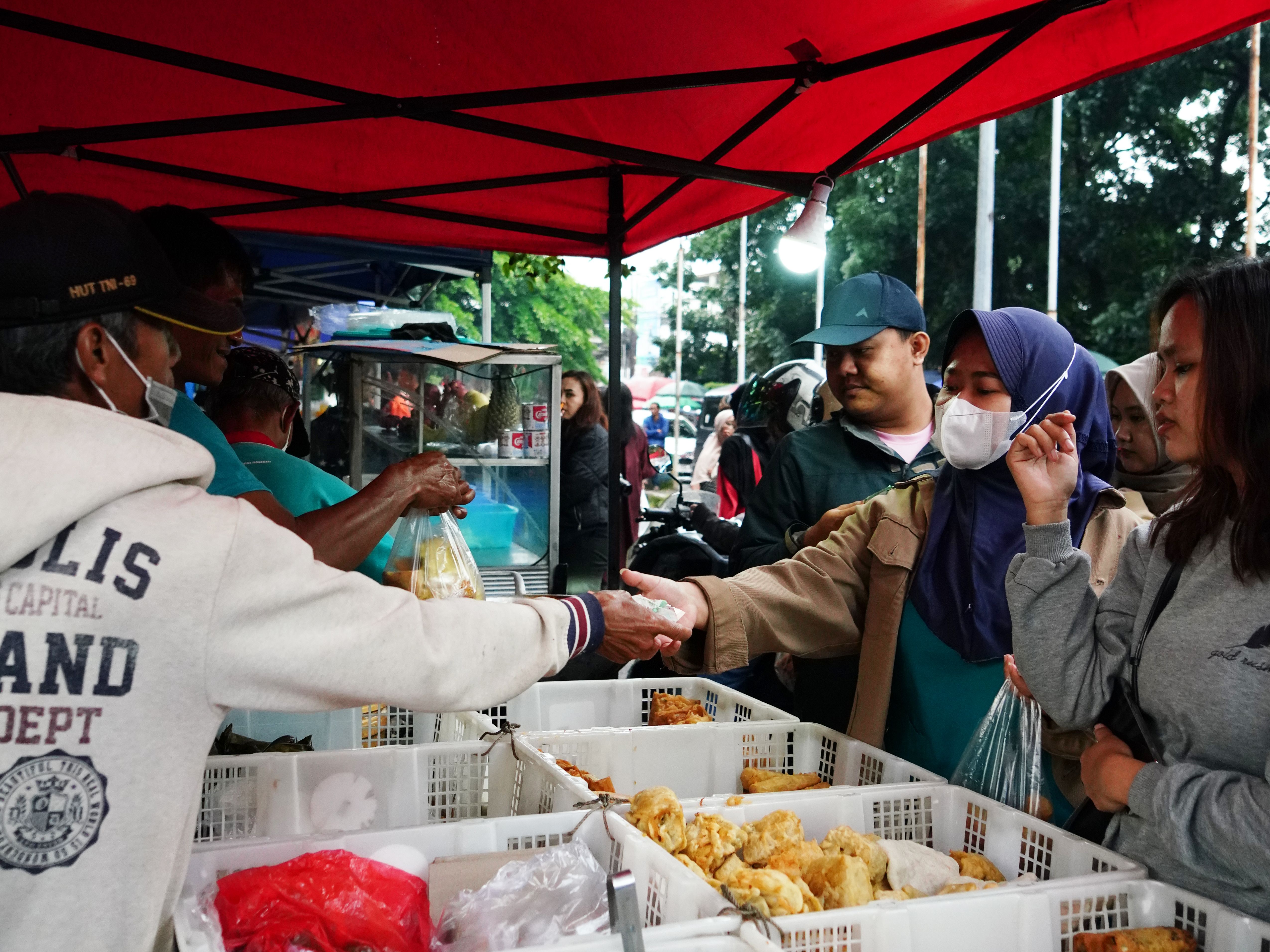 People shopping at a vibrant local street food market in Jawa Barat, Indonesia, under colorful tents.