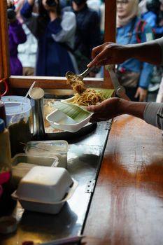 Street vendor prepares a traditional Indonesian meal in a busy market setting.