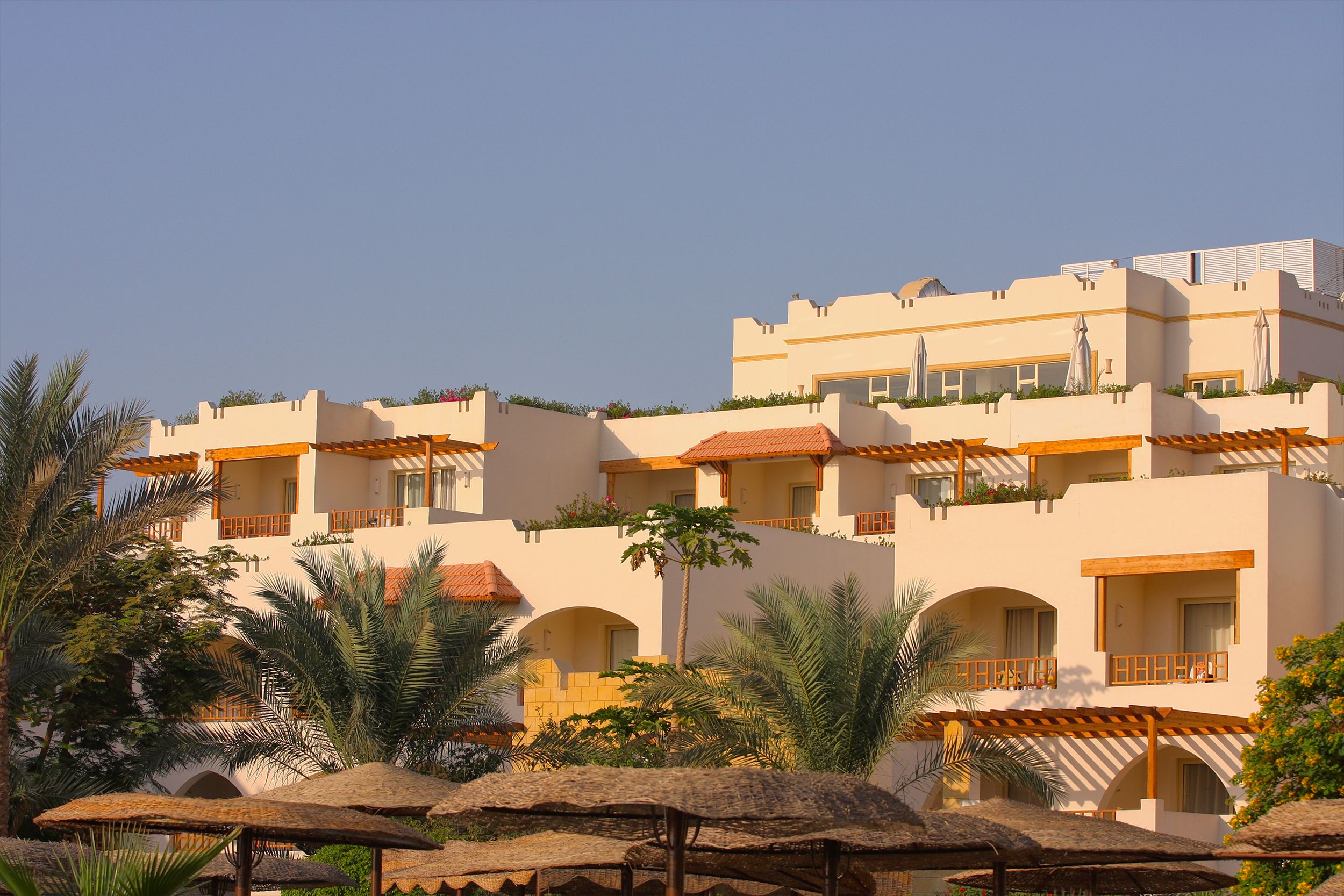 Bright resort building with palm trees under a clear blue sky, showcasing Mediterranean architecture.