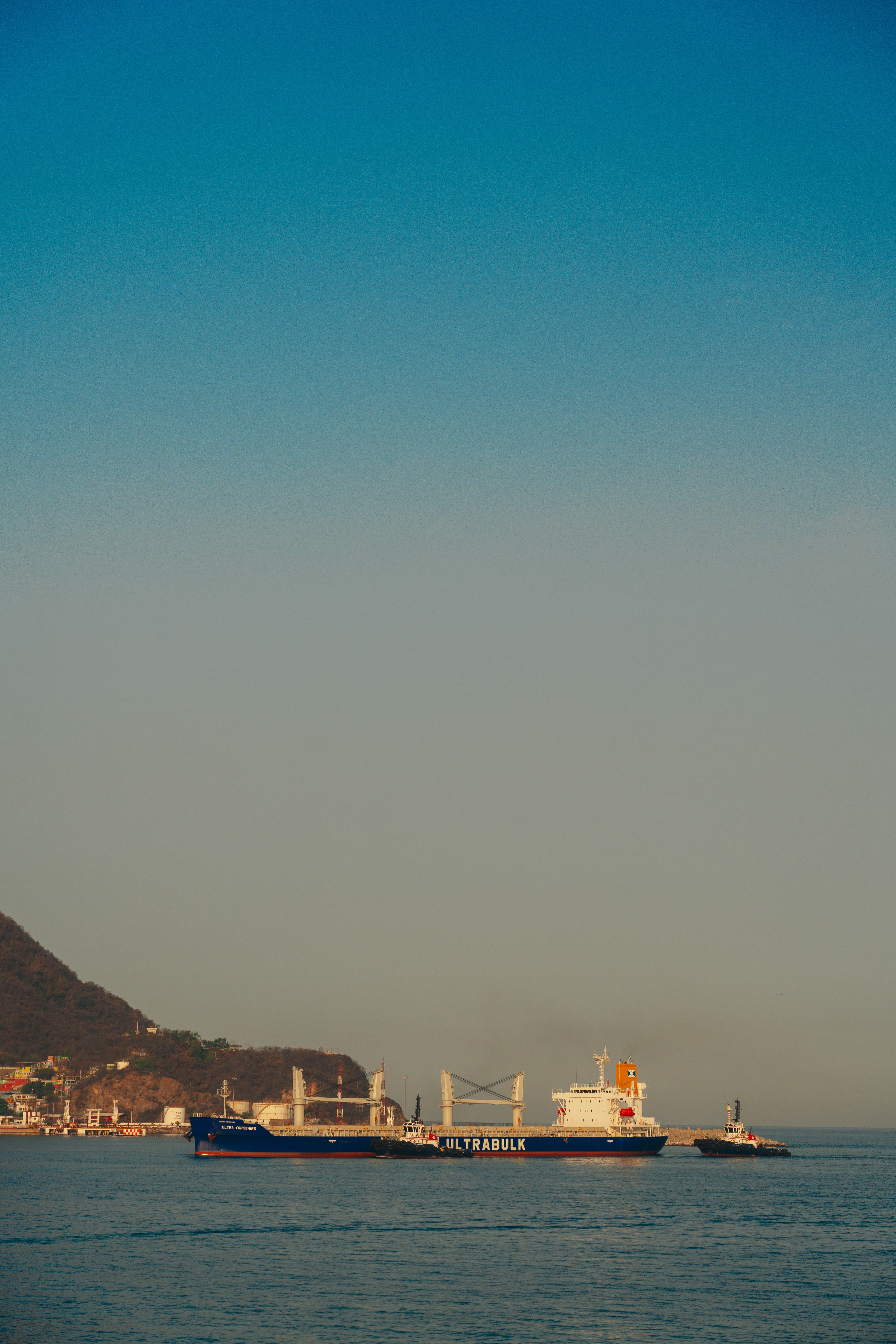 A feeder container ship berthed at a coastal port with gantry cranes loading containers