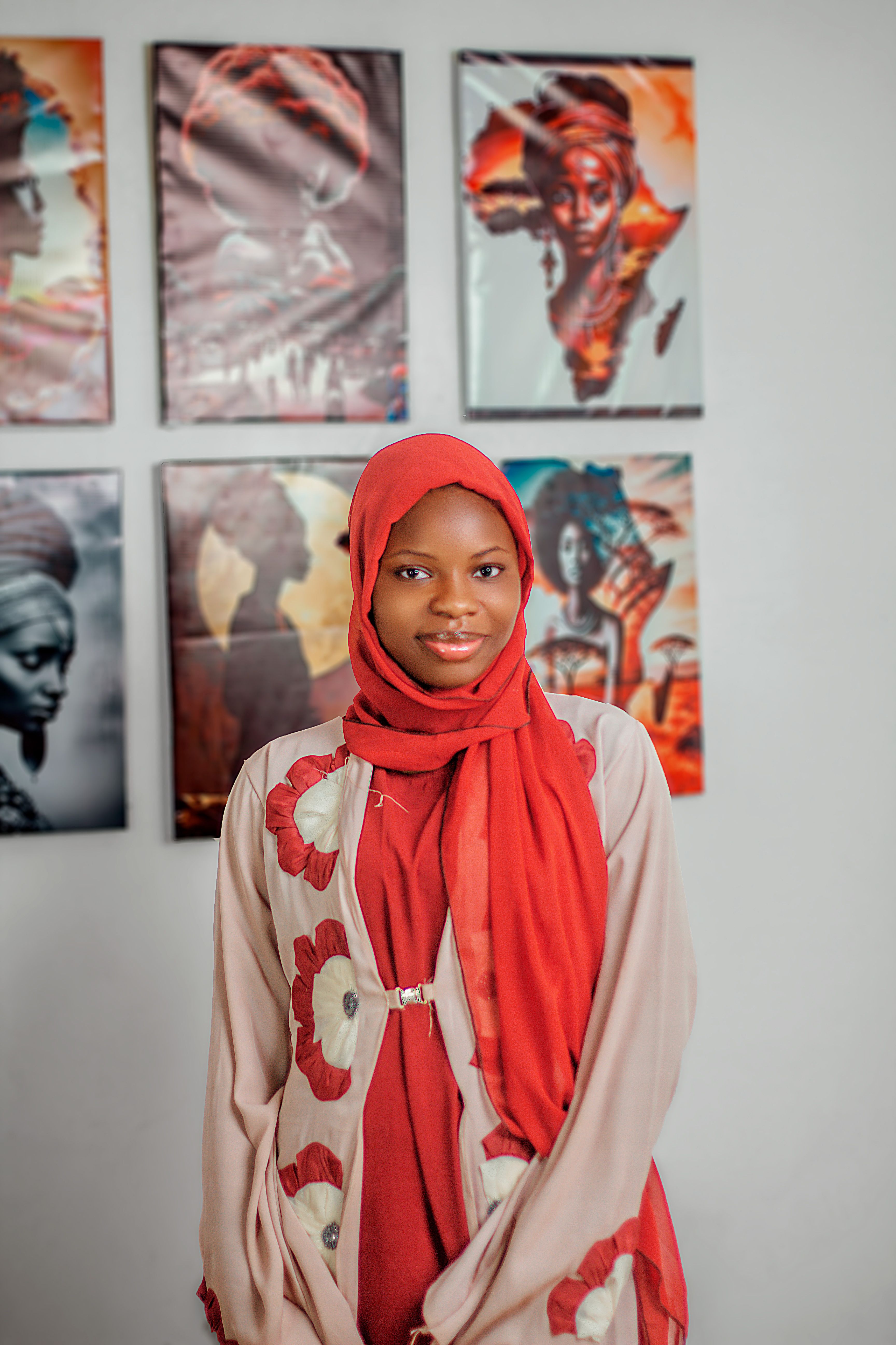 Young woman in a red headscarf smiles, standing in front of artistic portraits.