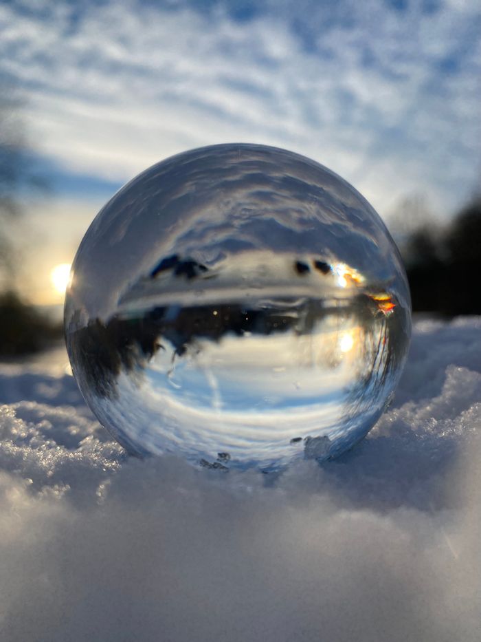 A glass sphere resting in snow, inverting the landscape behind it — photo on Pexels
