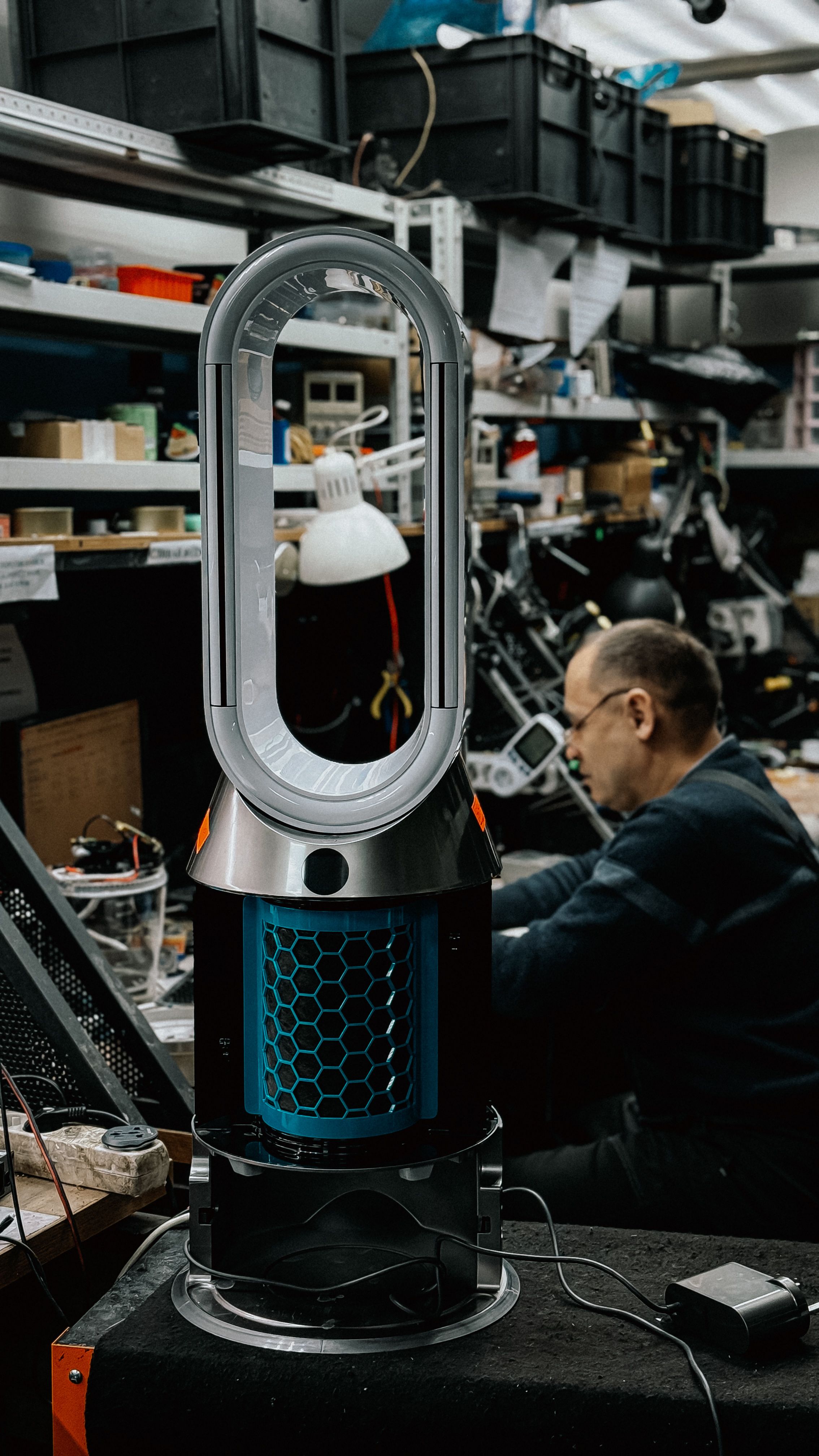A sleek air purifier on a workbench in a busy repair workshop, surrounded by tools and gadgets.