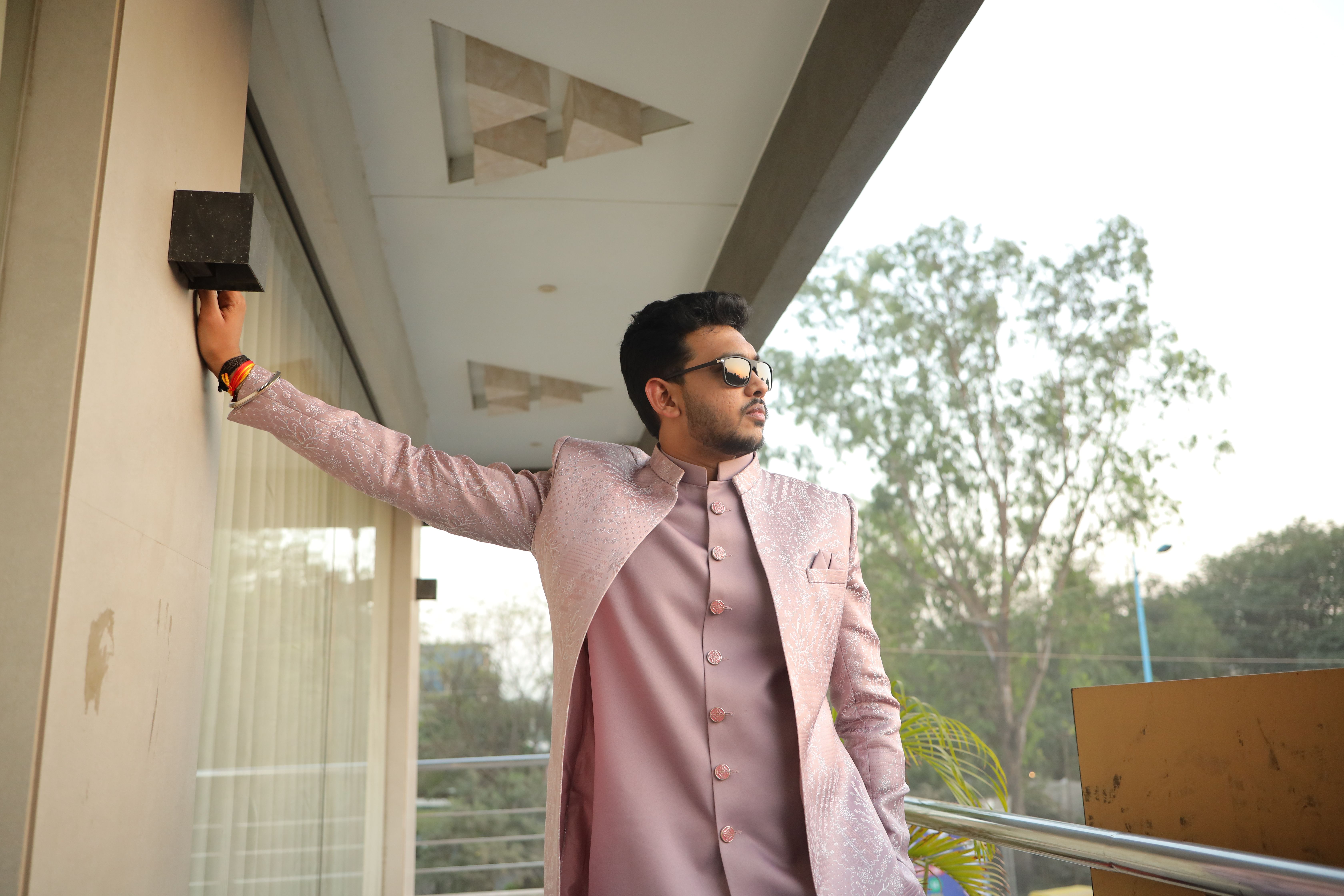 Man in elegant traditional attire confidently posing on a balcony, outdoors.