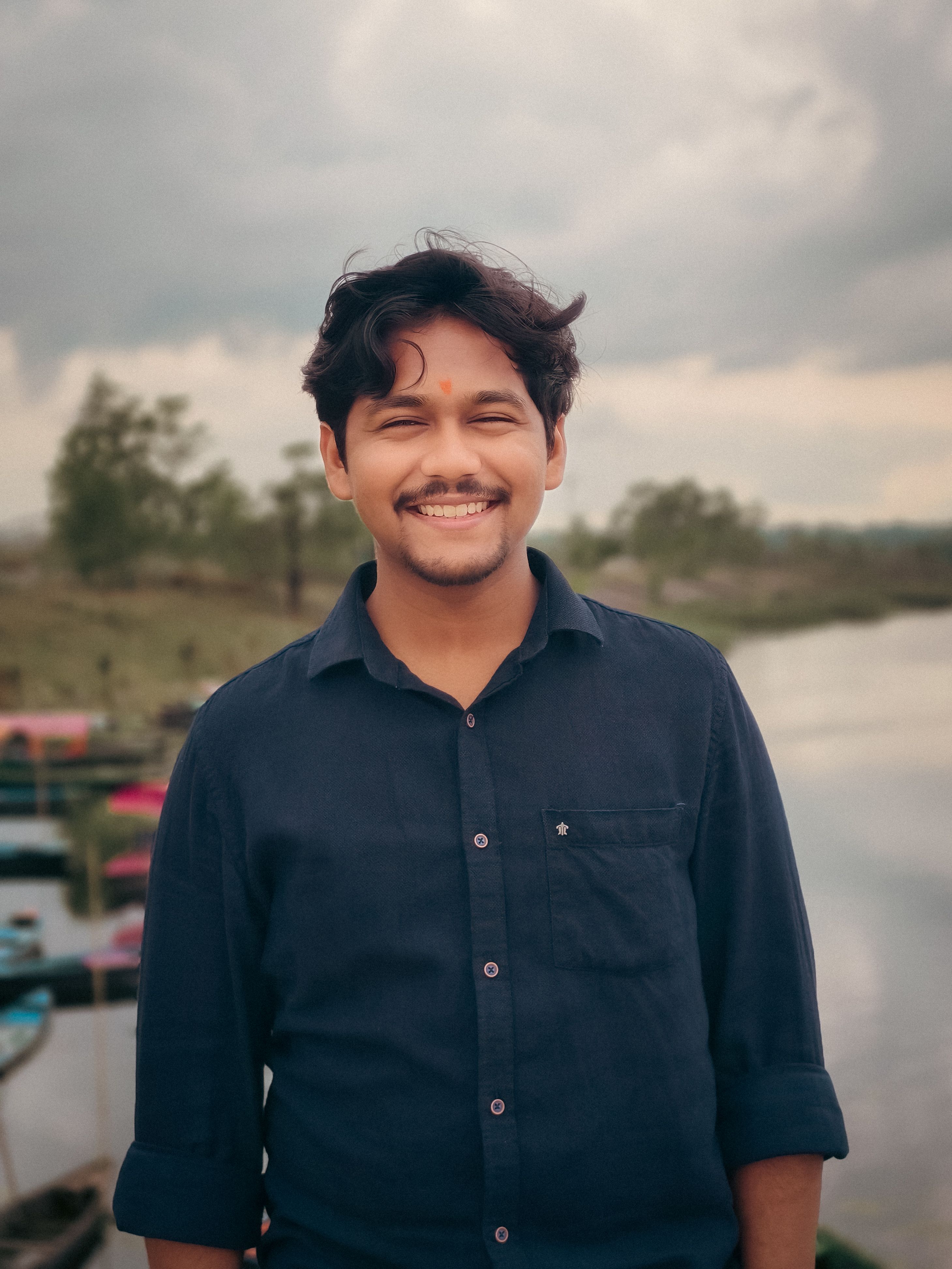 A cheerful young man smiling by a lakeside, capturing a serene outdoor moment.