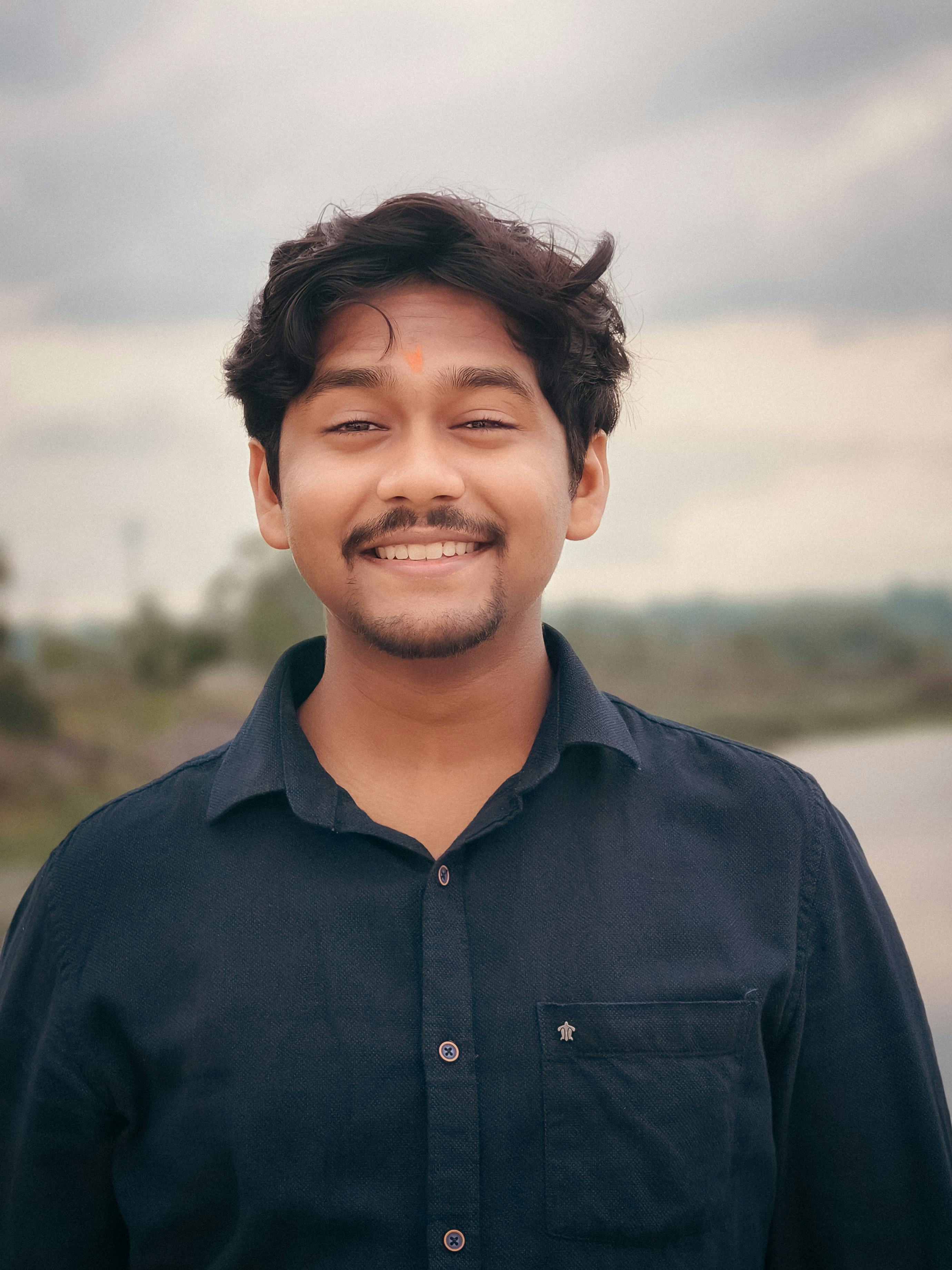 Portrait of a smiling young man outdoors with cloudy sky background.