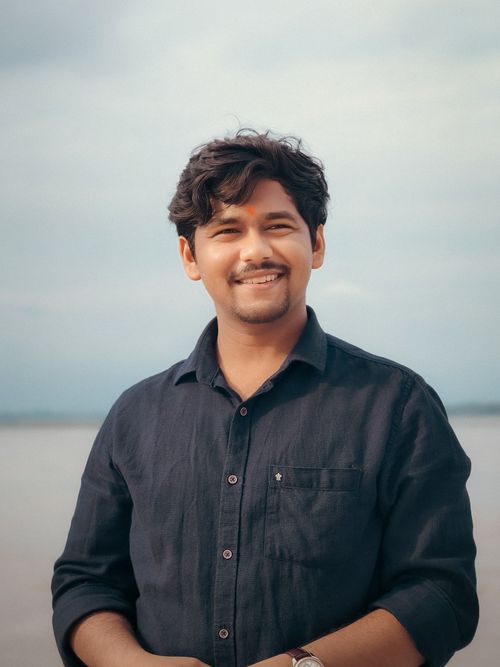 Free A smiling man stands outdoors with a scenic background of water and sky, conveying a warm and relaxed atmosphere. Stock Photo