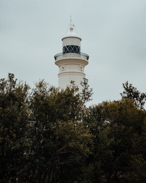 White and Black Lighthouse Near Green Trees Under White Clouds