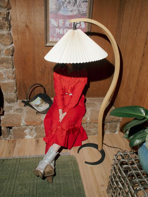 A woman in a red dress partially hidden by a lamp, creating a unique indoor visual.