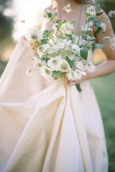 A bride in a gown holding a delicate bouquet of white flowers outdoors.